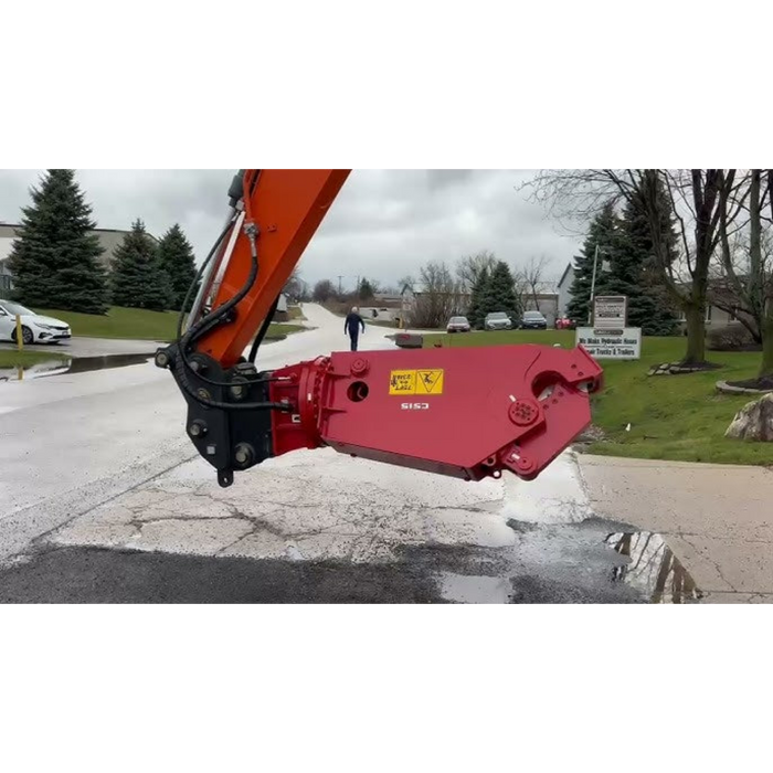 Red excavator attachment on a street with a cloudy sky and trees in the background.