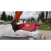 Red excavator attachment on a street with a cloudy sky and trees in the background.