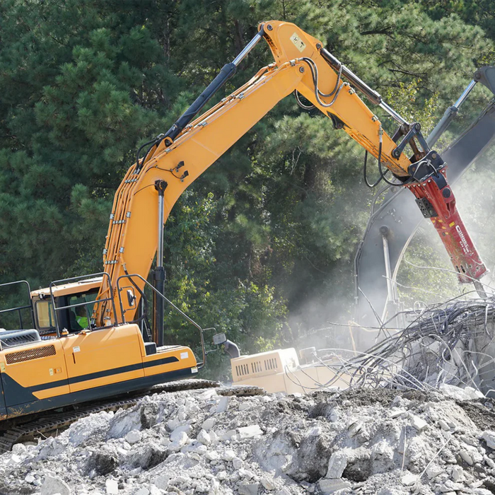 Yellow excavator demolishing concrete blocks with trees in the background using Connect Work tools hydraulic breaker