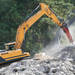Yellow excavator demolishing concrete blocks with trees in the background using Connect Work tools hydraulic breaker