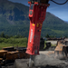 Red hydraulic breaker with "Connect Work Tools" branding against a mountainous landscape.