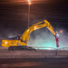 Yellow excavator with a red demolition hammer on a road at night