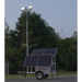 Solar-powered light tower with a solar panel on a trailer in a forest setting.