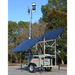 Mobile lighting tower with solar panels on a trailer in an outdoor setting.