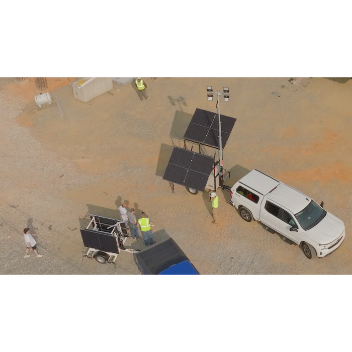 Solar security camera tower with flood lights and solar panels on a trailer hitched to white truck and people in a construction jobsite setting 
