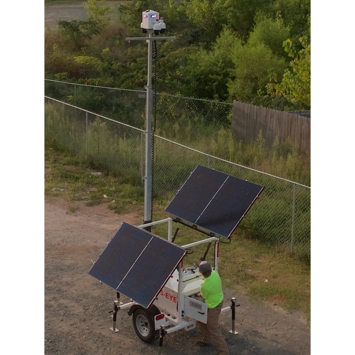 Solar-powered security camera trailer with two large solar panels, with a person operating it outdoors.