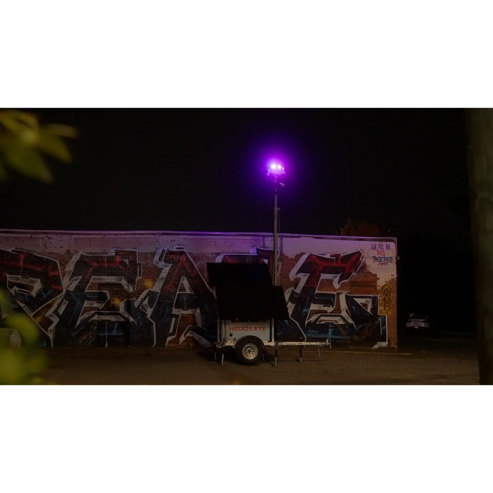 Solar security camera trailer parked in front of a graffiti-covered wall with a red/blue light in the background.