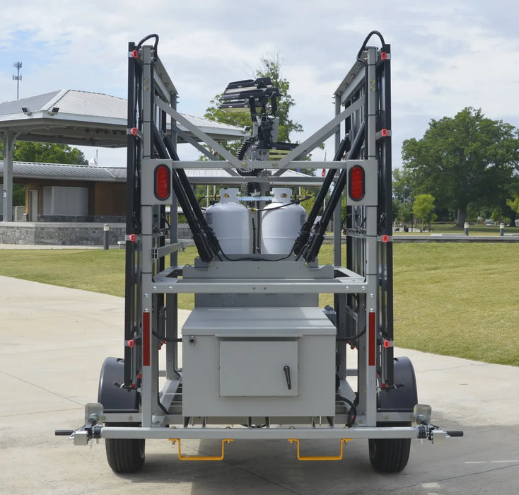 Mobile solar/hybrid light tower with two propane containers on a paved area with greenery in the background