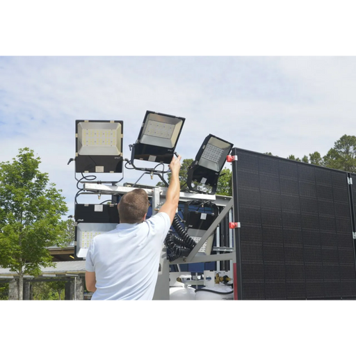 Person adjusting outdoor flood lights on a mobile light tower with outdoors background
